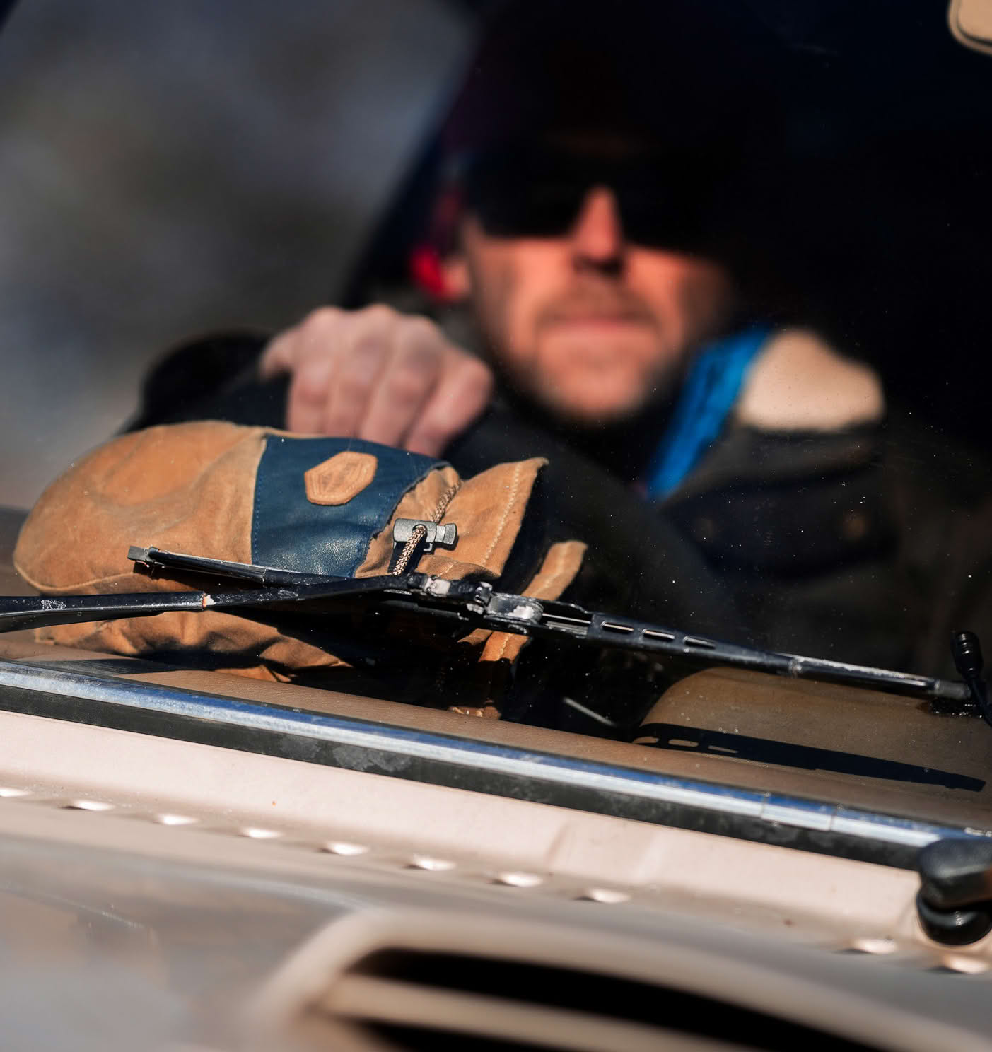 Man wearing sunglasses and gloves driving a vehicle, seen through the windshield with a focus on the wiper mechanism.