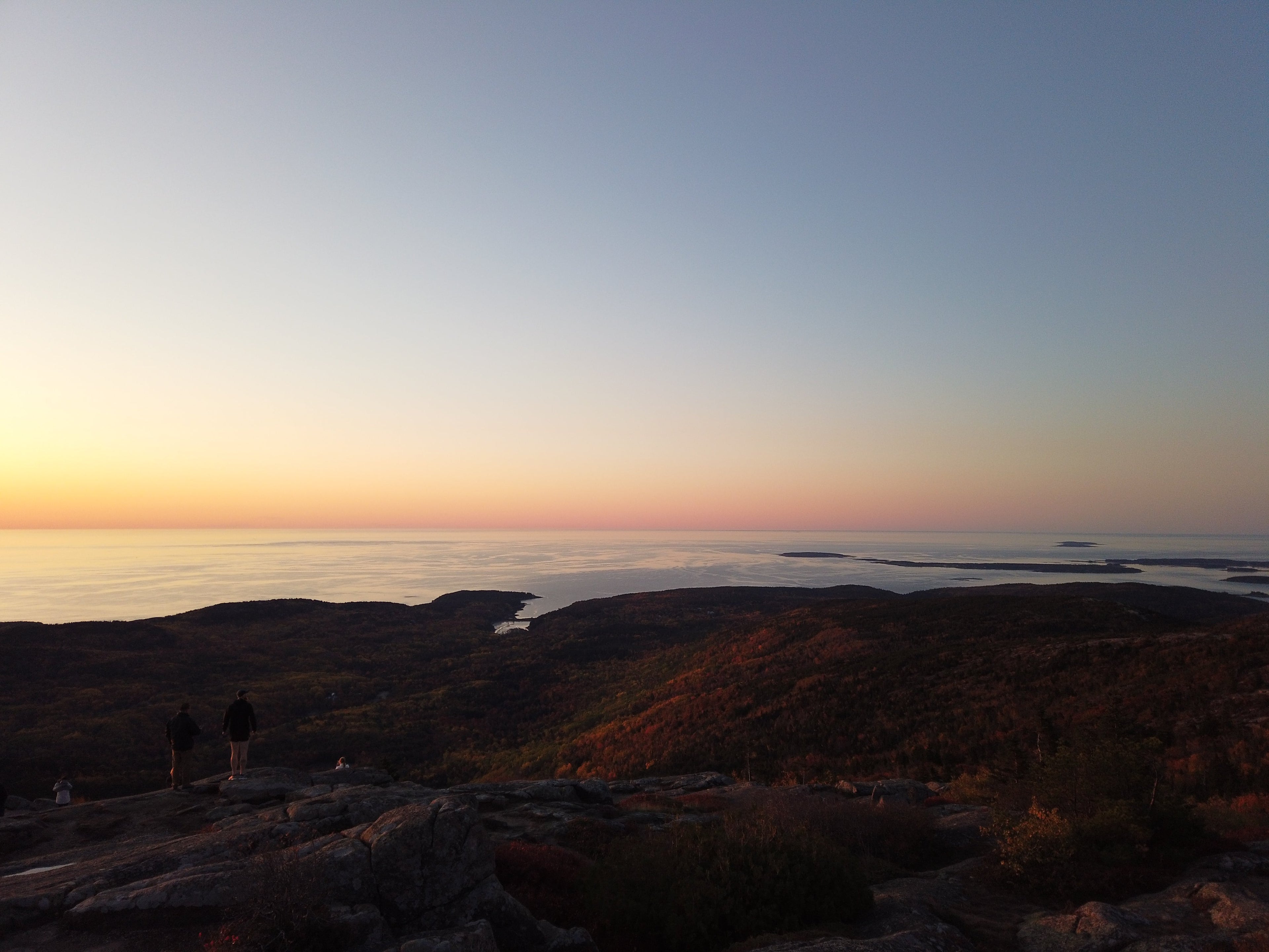 Two people standing on top of a mountain at sunset.