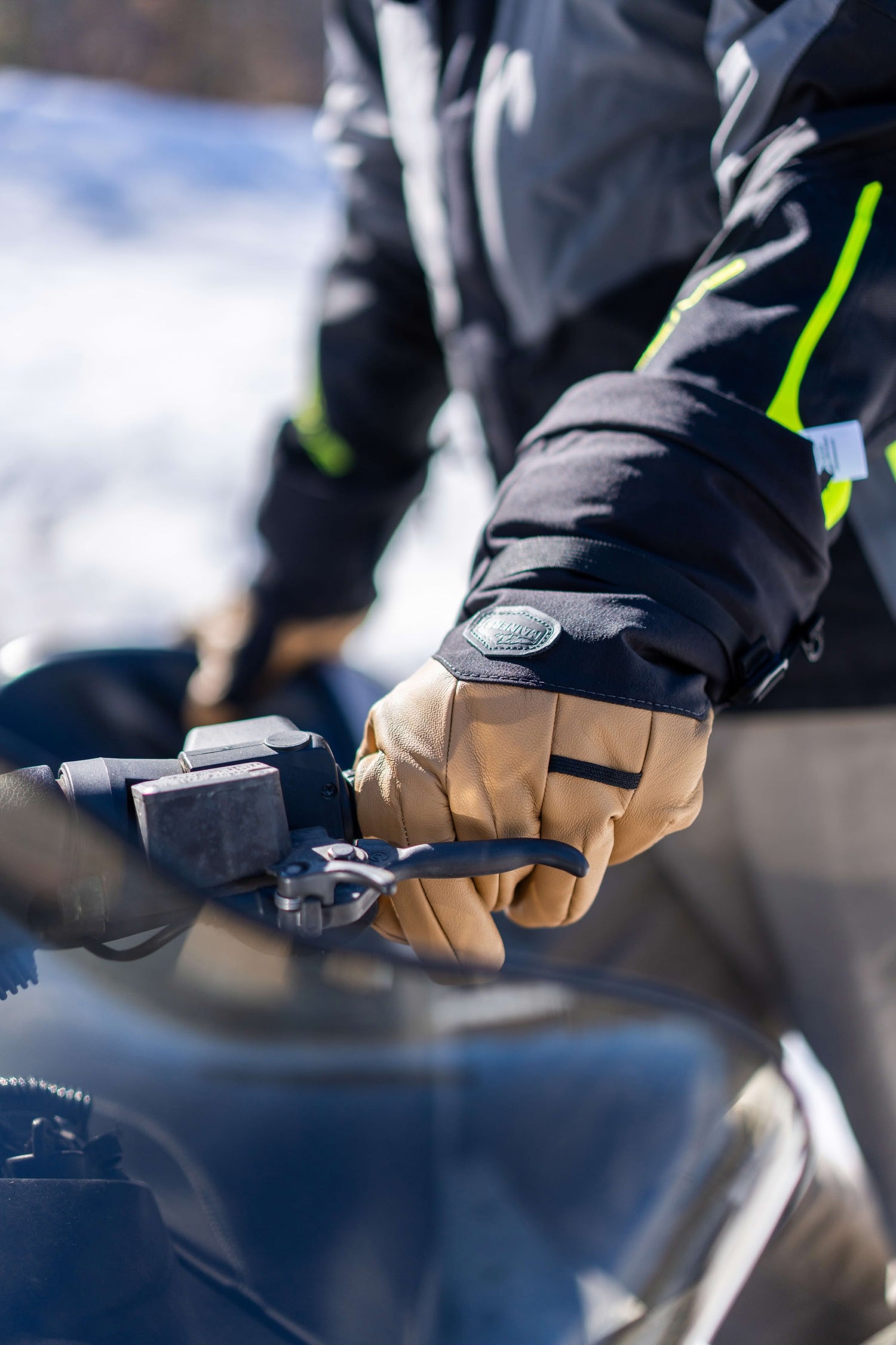 Person wearing beige gloves operates a black handlebar on a snowy day.