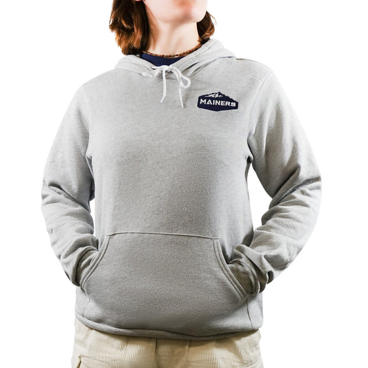 A woman wearing a soft, grey Mainers Hoodie with a logo on it.
