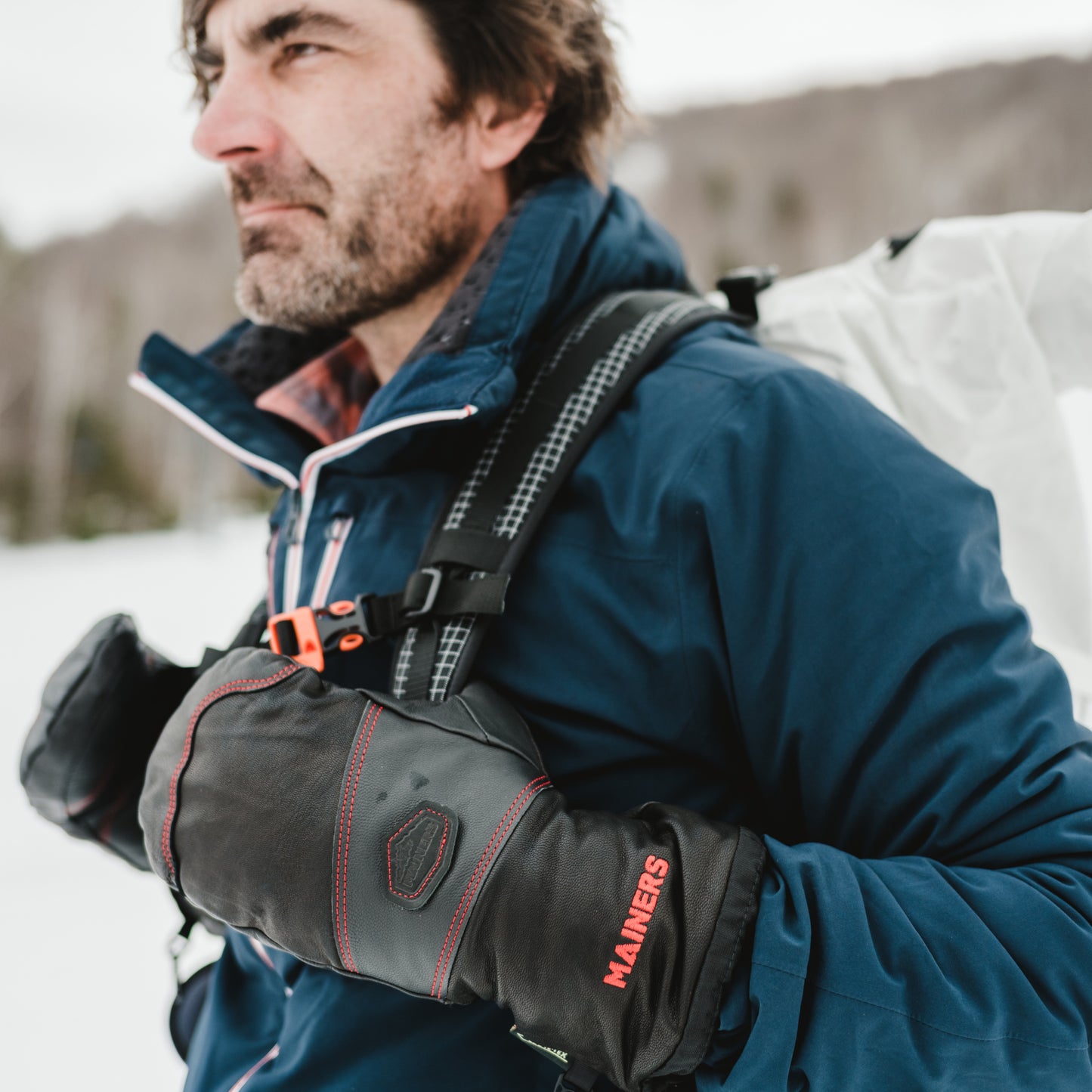 A man wearing a blue jacket and Mainers All-Leather Mitts gloves.