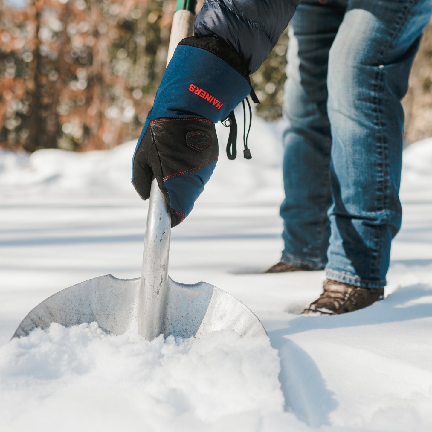 A person with a Mainers Mitts-clad hand holding a shovel in the snow.