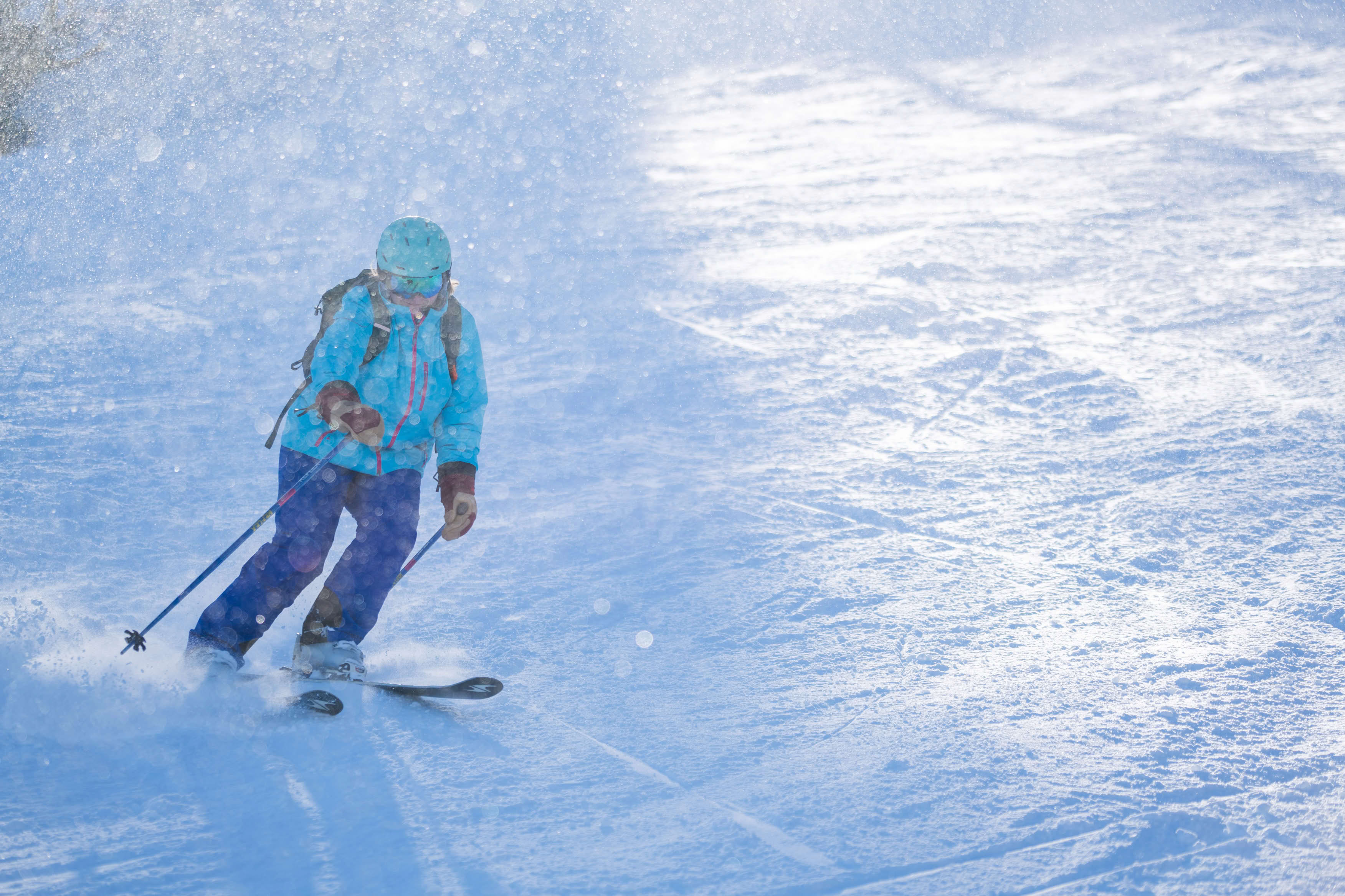 A person skiing downhill on a snowy slope, wearing a teal jacket and helmet, with ski poles in hand.