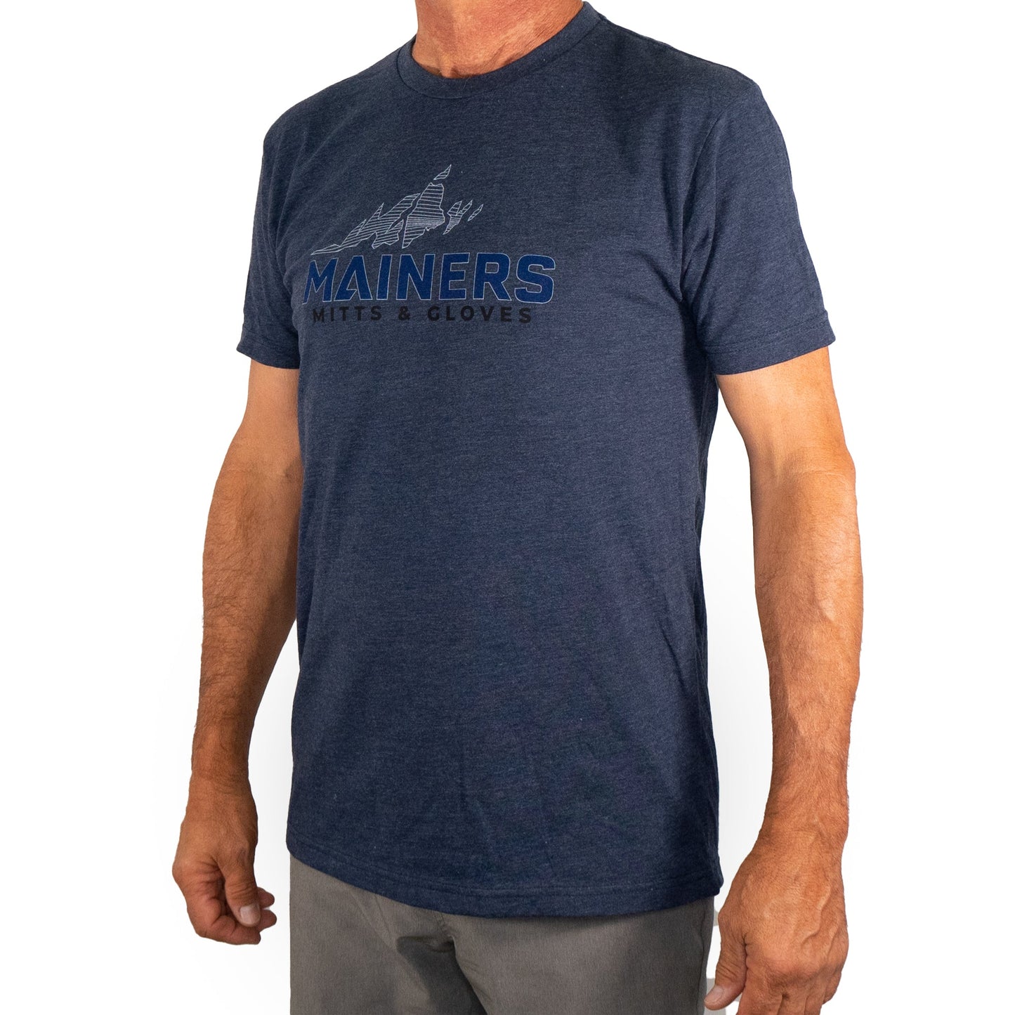 A person wearing a Mainers MG Tee in navy blue, featuring "Mainers Mitts & Gloves" and a mountain graphic, perfectly embodies a spirit of adventure and passion for outdoor exploration.