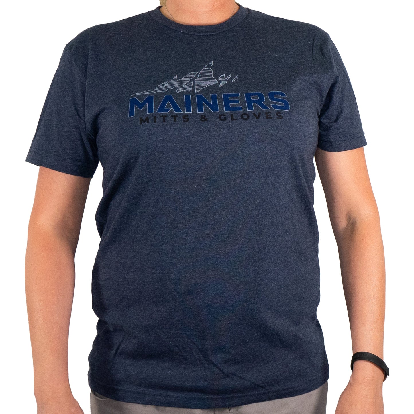 A person wearing a Mainers MG Tee in dark blue, featuring "Mainers Mitts & Gloves" prominently displayed, radiates an adventurous spirit ideal for outdoor exploration.