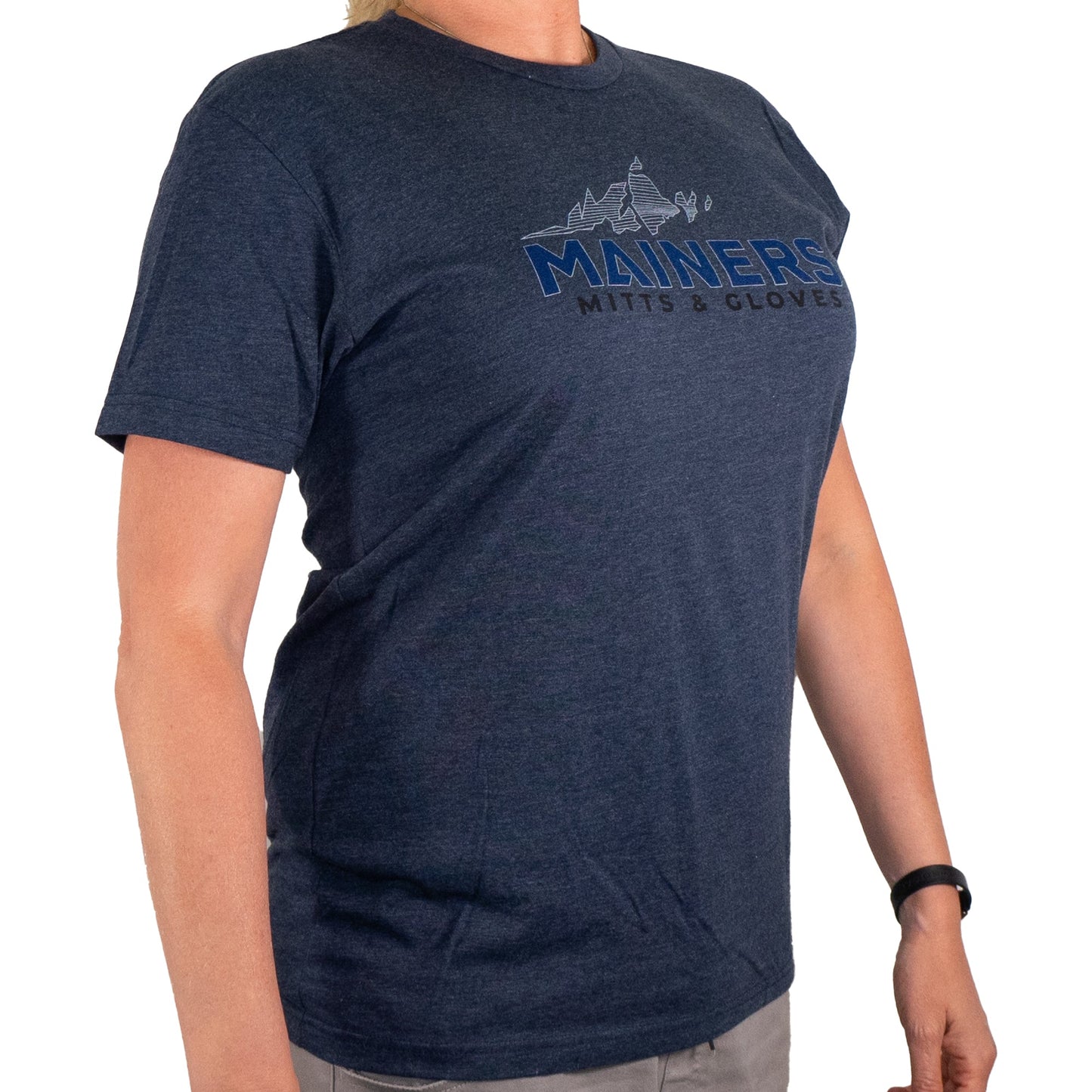 Adorned for outdoor adventures, this explorer sports a navy Mainers MG Tee featuring the "Mainers Mitts & Gloves" logo, paired with light gray pants and an elegant black wristband.