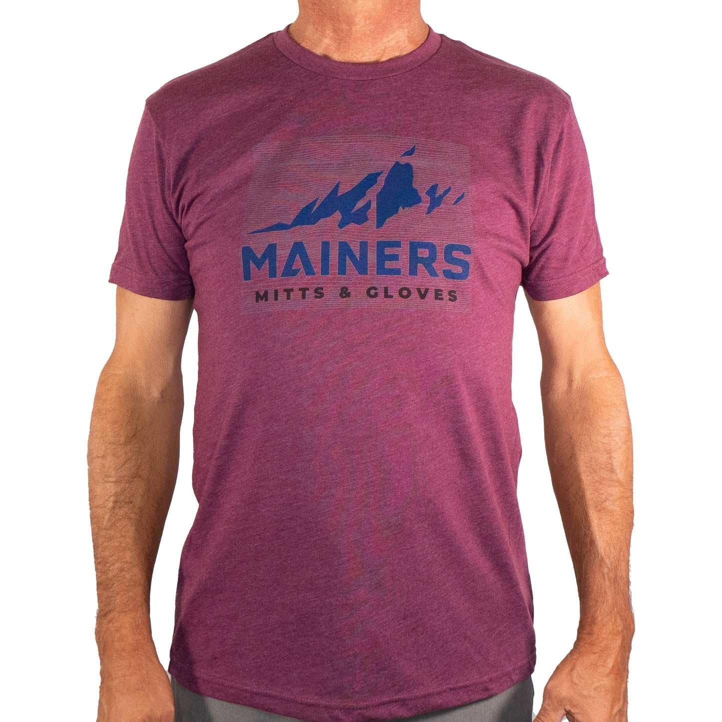 A person dons an adventurous spirit in a maroon Mainers Ridge Line Tee featuring a mountain graphic, boasting a comfortable fit for any journey.