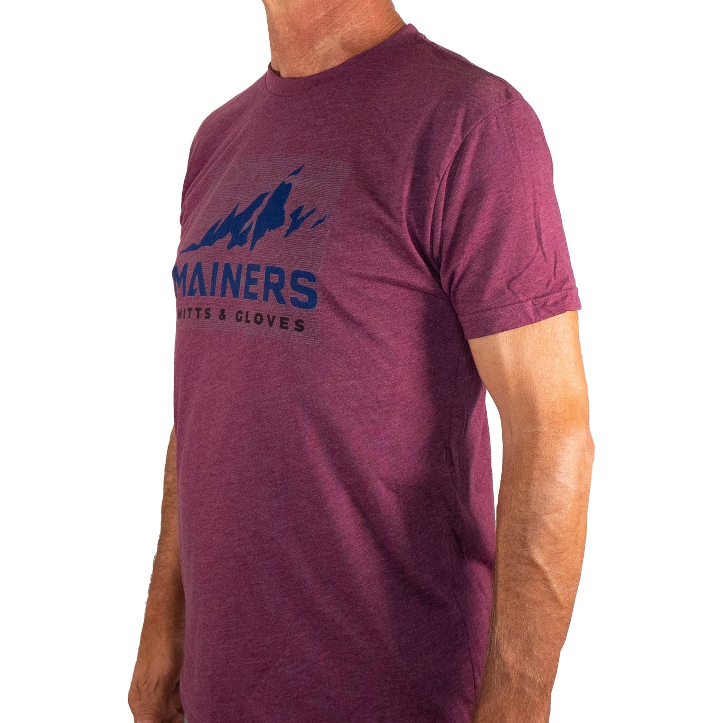 A person wearing a Mainers Ridge Line Tee featuring a mountain graphic and the brand name "Mainers" stands against a plain white background, highlighting its adventurous spirit and comfortable fit.