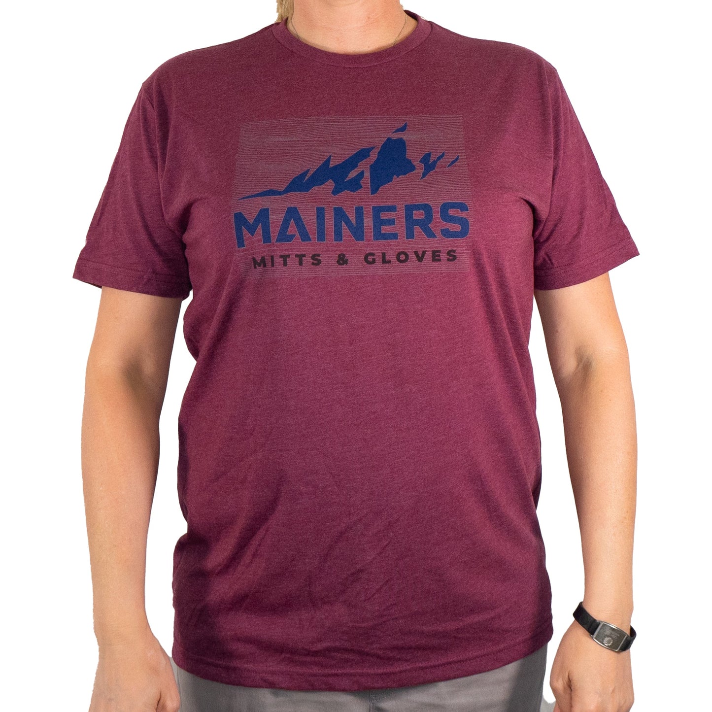 A person wears the Mainers Ridge Line Tee, a maroon T-shirt with a mountain design and the brand name "Mainers," embodying an adventurous spirit while ensuring a comfortable fit.
