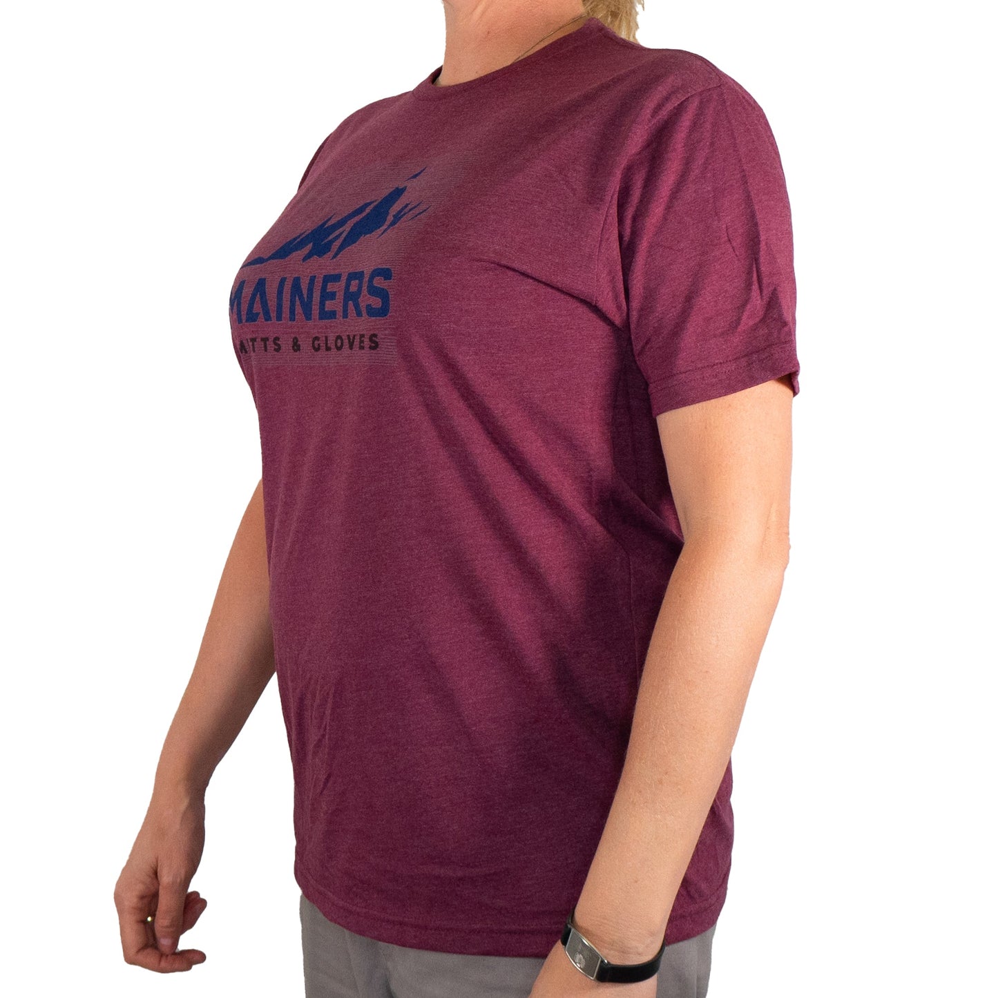 An individual wearing the Mainers Ridge Line Tee, featuring a mountain logo and text that epitomizes an adventurous spirit, stands against a white background.