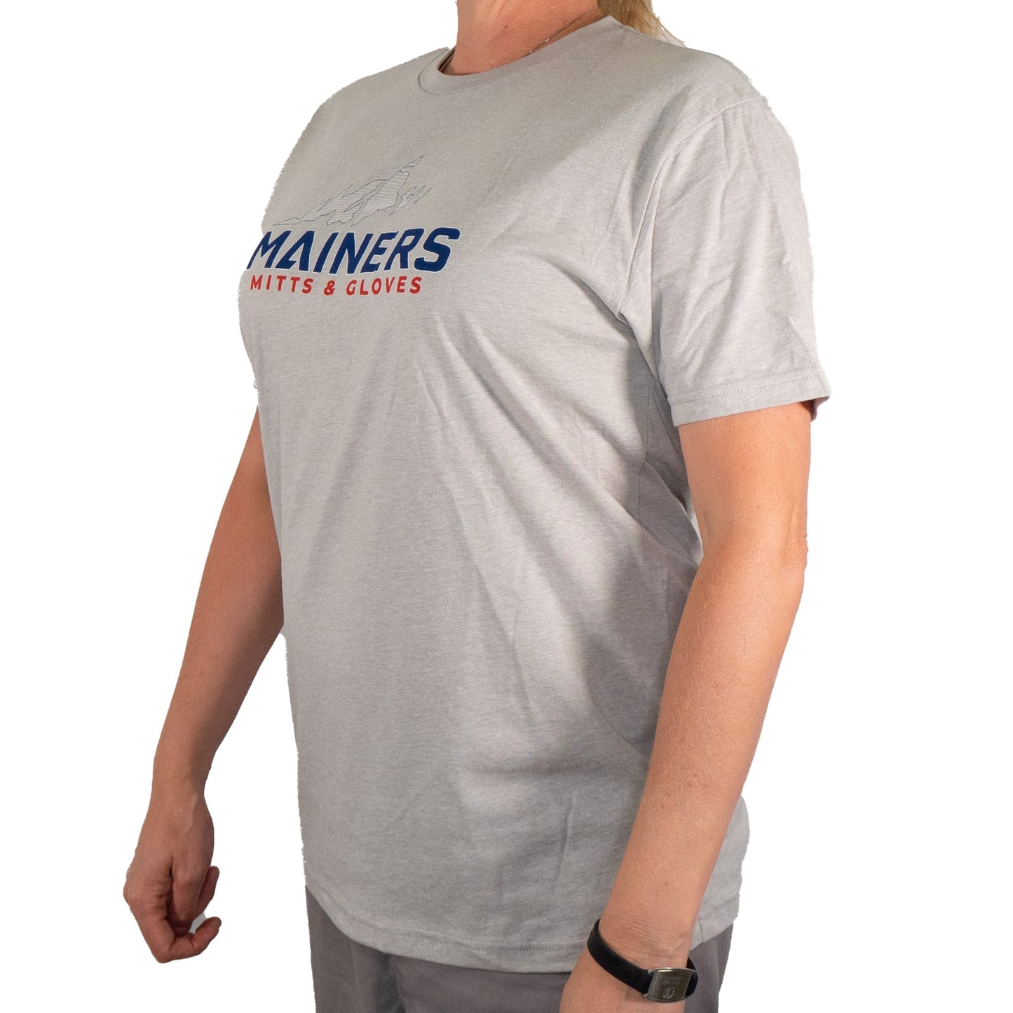 A person sporting a Mainers MG Tee in gray is set for an outdoor adventure, with the phrase "Mainers Mitts & Gloves" emblazoned on the front, embodying their adventurous nature.