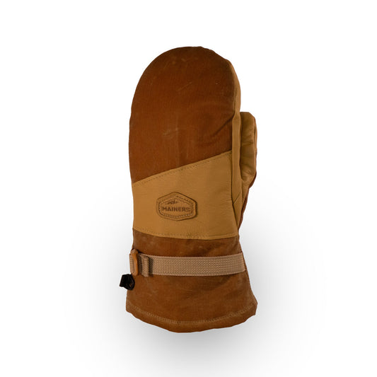 The Acadia Mitts by Mainers showcase a stylish brown and tan design, complemented by a buckle strap and a hexagonal logo patch on the back. They provide warmth and comfort, with their waxed canvas construction ensuring exceptional durability.