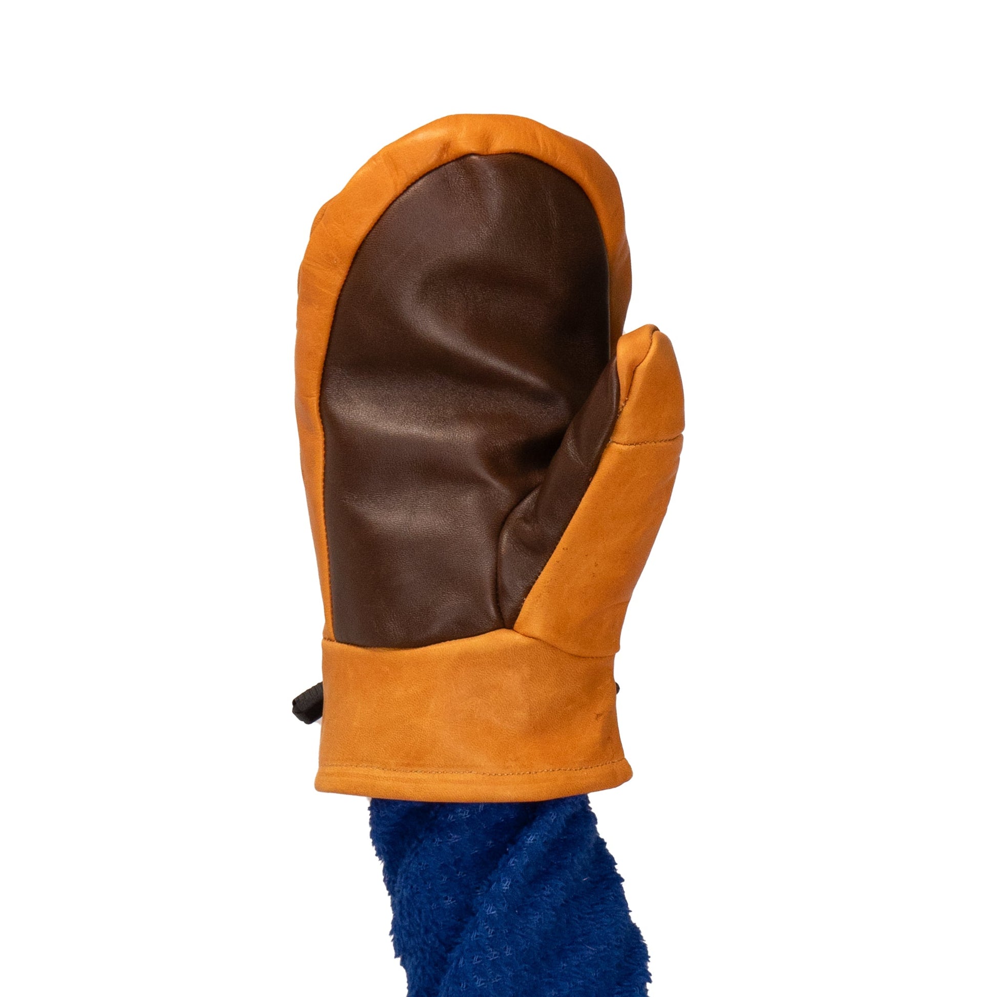 A person wearing a blue fuzzy sleeve holds up a brown and orange Portland All-Leather Mitt from Mainers, showcasing Maine craftsmanship, a wool-pile lining, and a separate section for the thumb.