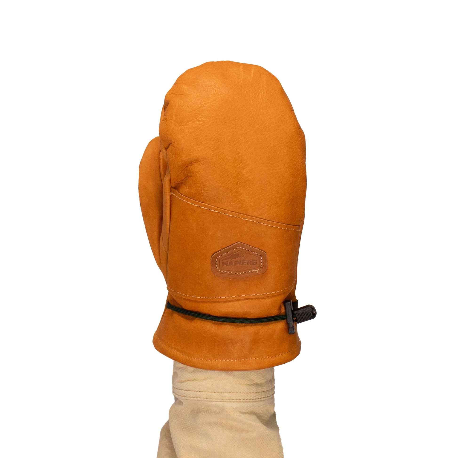 A person wearing Portland All-Leather Mitts by Mainers, crafted in tan leather with a drawstring closure. These mitts highlight exceptional Maine craftsmanship, featuring a logo patch on the back and a cozy wool-pile lining for enhanced comfort.