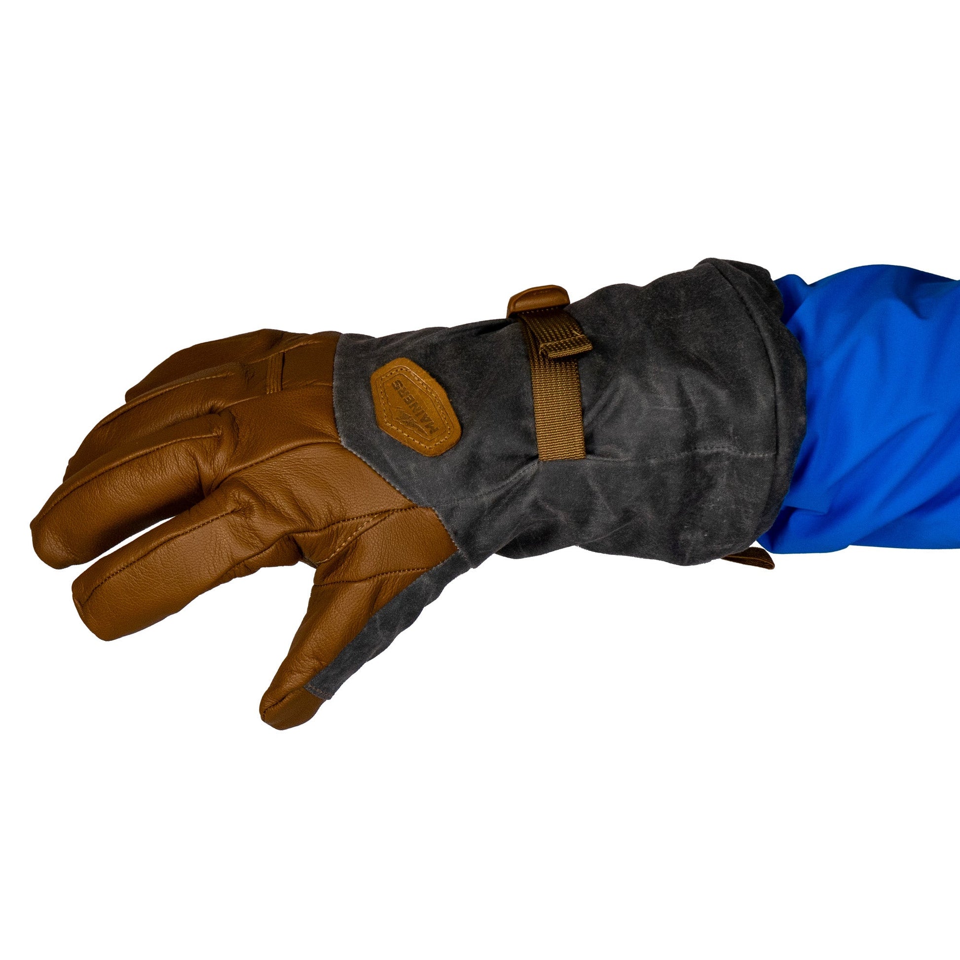 Close-up of a gloved left hand in a blue sleeve. The Mainers Bethel Glove, made with waxed canvas, showcases a brown finish paired with a dark fabric overlay and is equipped with a buckle strap for improved outdoor performance.