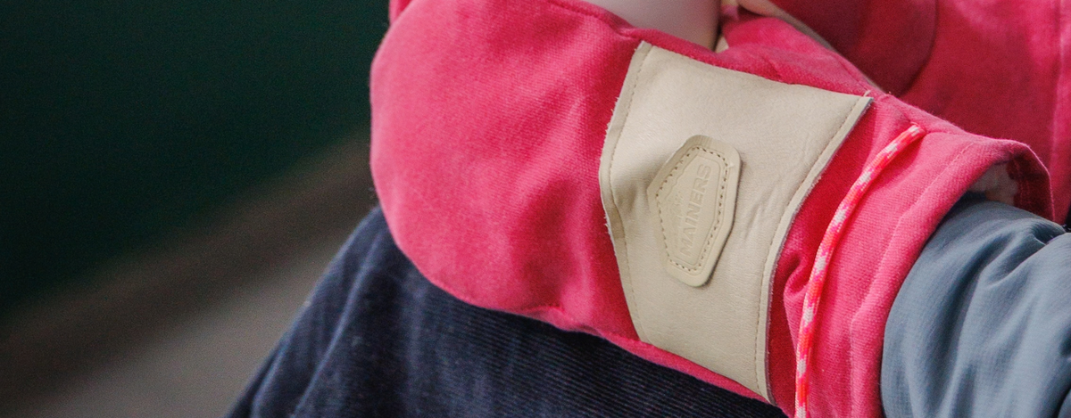 A close-up of a person wearing a pink winter mitt with a white fabric patch on the back, paired with a gray long-sleeve shirt.