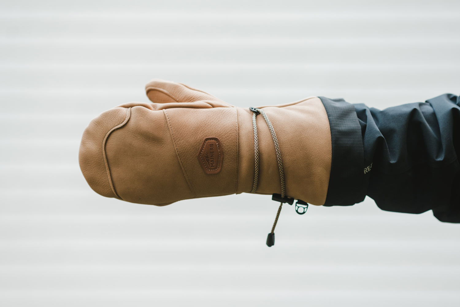 A person is holding a warm tan leather Mainers Caribou Mitt.