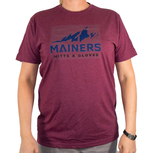 A person wears the Mainers Ridge Line Tee, a maroon T-shirt with a mountain design and the brand name "Mainers," embodying an adventurous spirit while ensuring a comfortable fit.